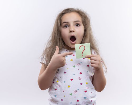 surprised little school girl wearing white t-shirt points to paper question mark on isolated white background